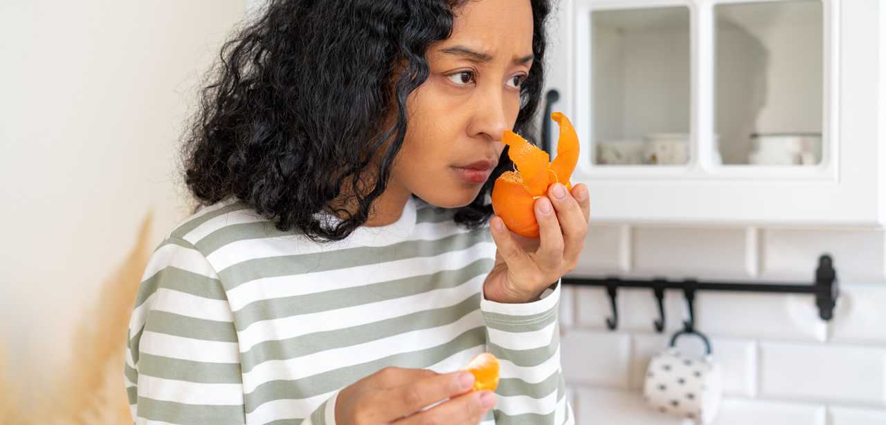 Photo d'une femme illustrant les effets à long terme après avoir eu le coronavirus (perte d'odorat en sentant un fruit)