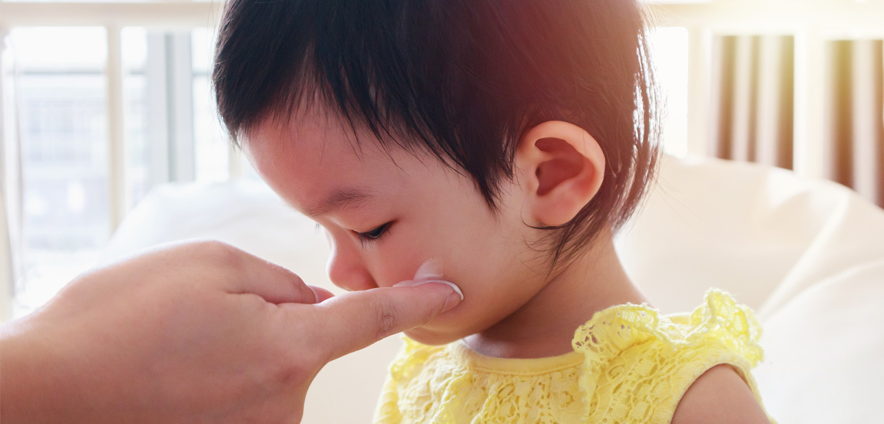 Un adulte applique une crème anti moustique sur le visage d'un jeune enfant