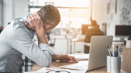 Photo d'une personne assis devant son bureau et qui se maintient le cou à cause de douleurs