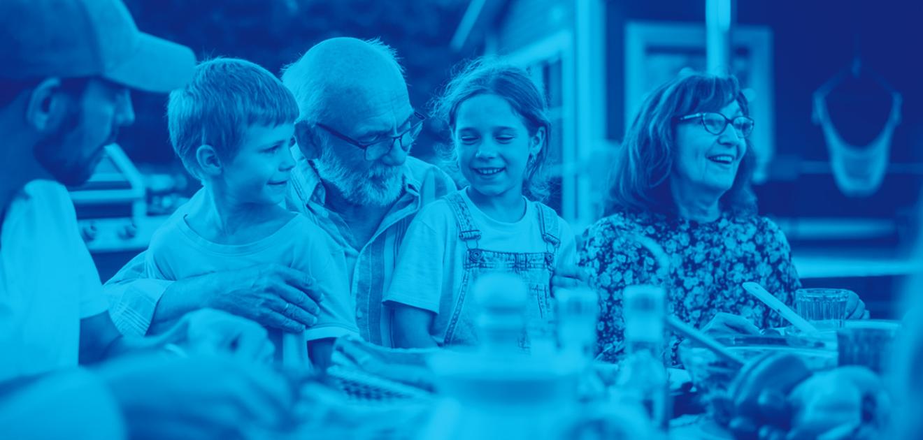 Portrait d'un grand-père aîné tenant ses petits-enfants sur les genoux lors d'un dîner en plein air.