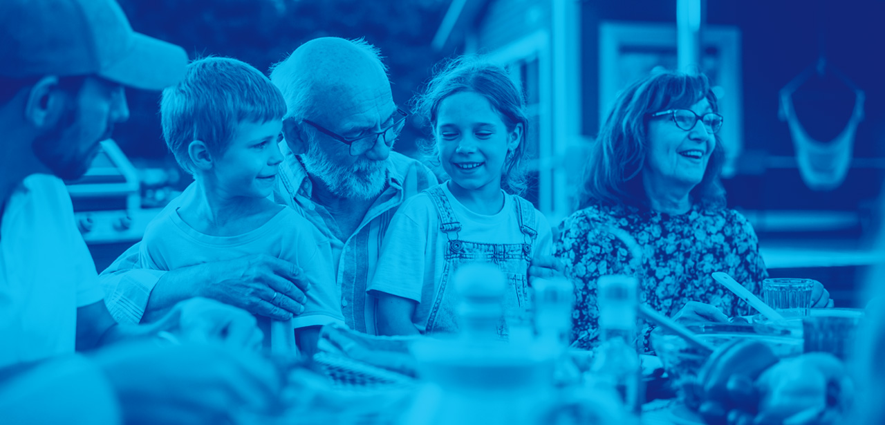 Portrait d'un grand-père aîné tenant ses petits-enfants sur les genoux lors d'un dîner en plein air.